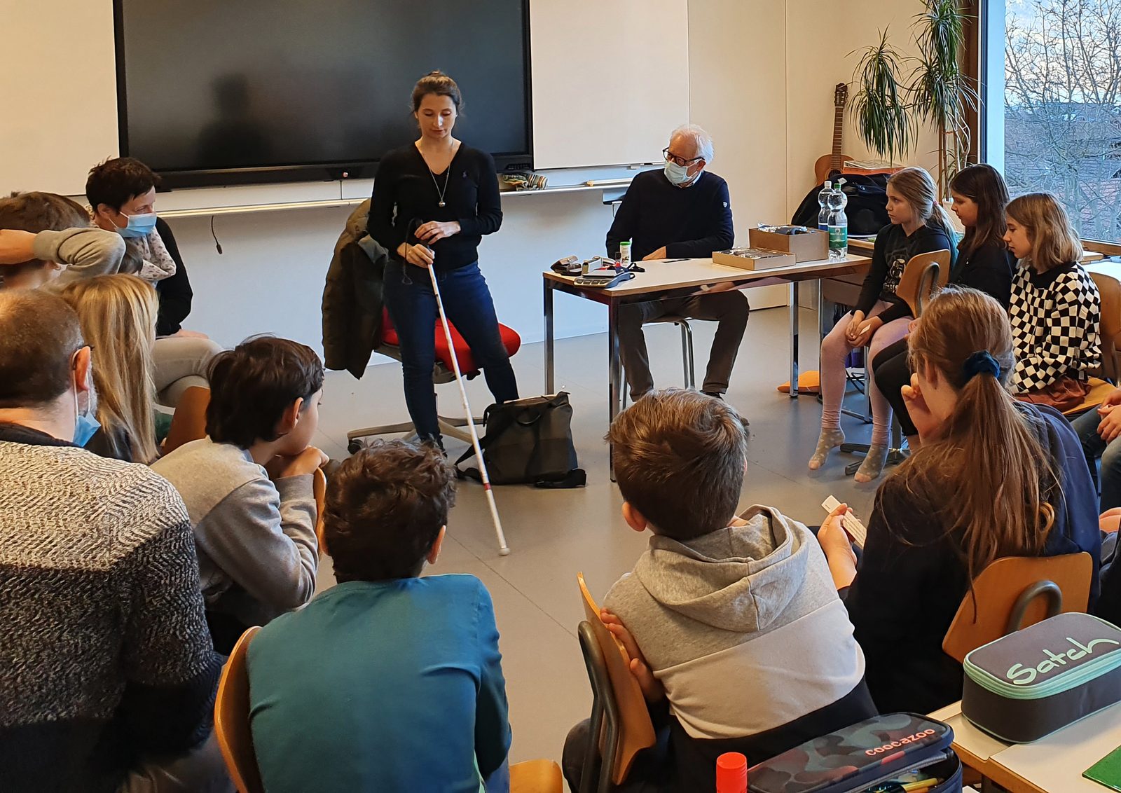 Schüler:innen probieren im Klassenzimmer mit Dunkelbrillen und Blindenstöcken das Gehen mit Sehbehinderung aus.